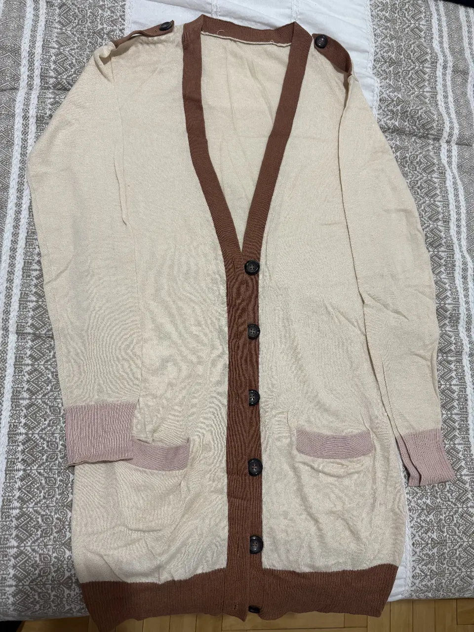 Cardigan largo de tejido color crudo con detalles marrones. Posee botones y bolsillos delanteros. Ideal para un look casual y abrigado.