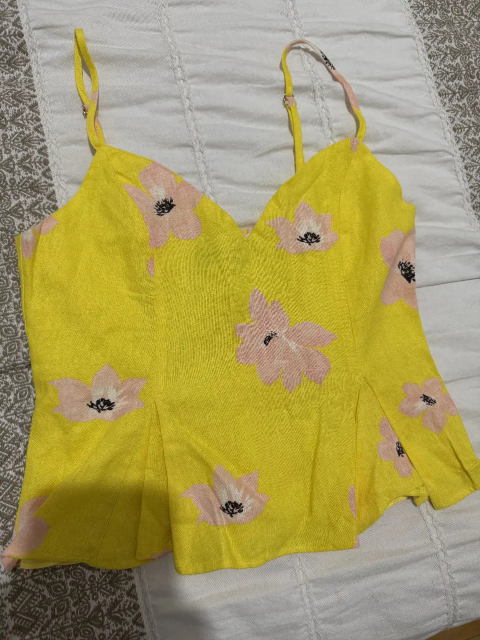 Top de lino amarillo con estampado floral rosa. Tiene tirantes finos ajustables y un diseño con frunces en la espalda. Ideal para un look fresco y femenino.