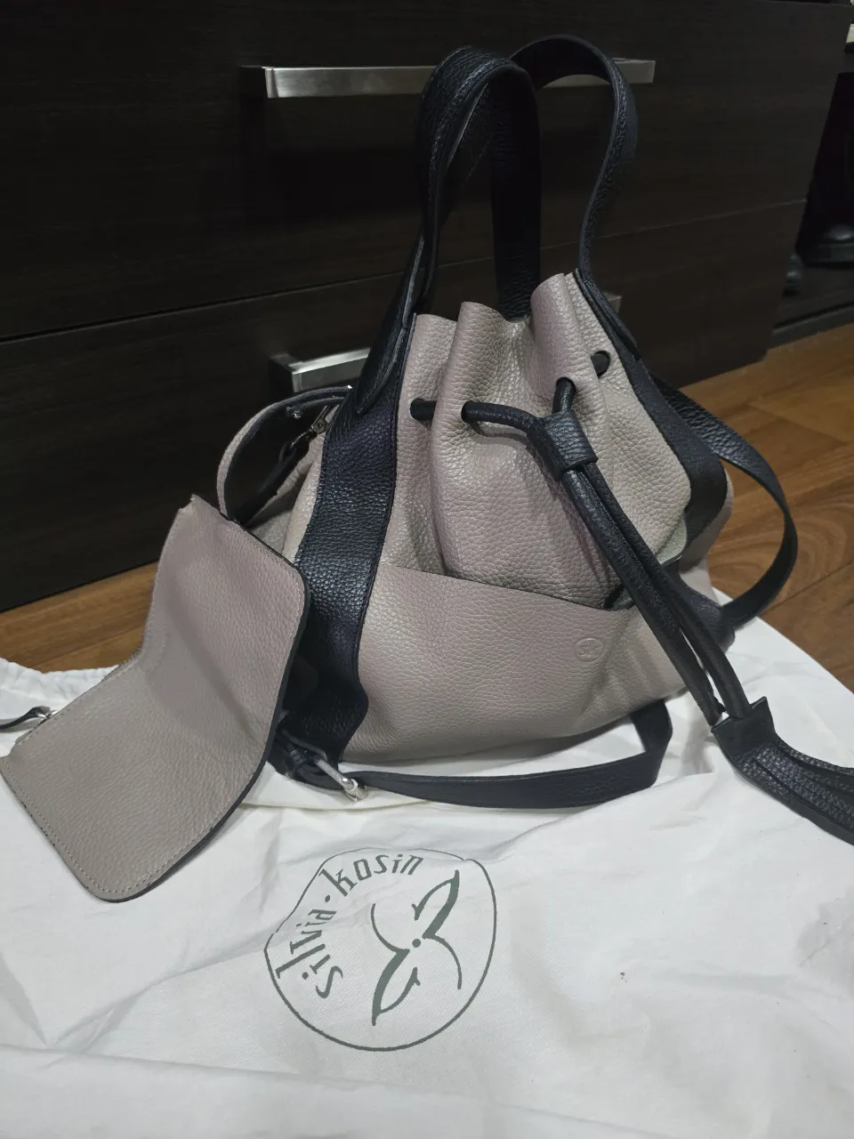 Bolso de cuero color gris y negro, con cierre de cordón y detalles de flecos. Incluye un pequeño monedero a juego. Ideal para el día a día.