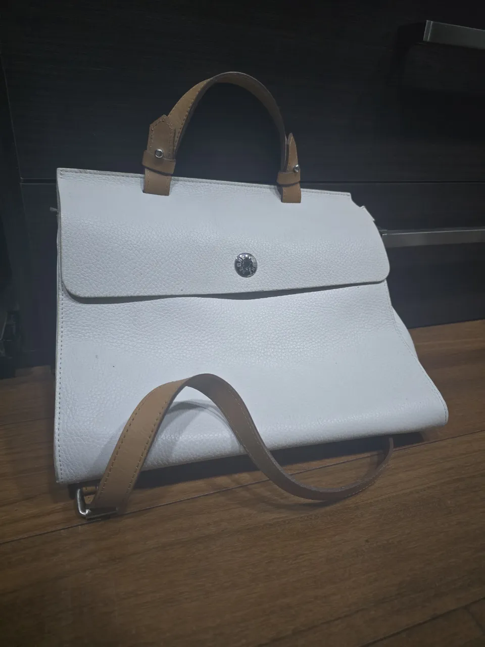 Bolso blanco de cuero con manijas y correa de cuero color suela. Tiene un bolsillo interno con cierre y un bolsillo externo con broche.