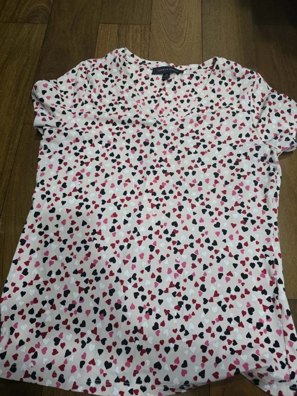 Remera súper linda y cómoda con estampa de corazones en varios tonos de rosa, rojo y negro sobre fondo rosa claro. Ideal para un look casual y tierno. Perfecta para el día a día o para salir con amigas.