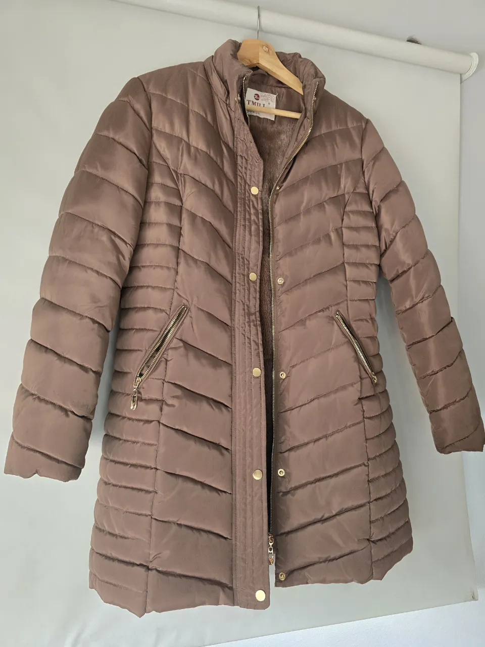 Campera impecable, 2 usos, acolchada marrón con interior de peluche. Tiene cuello alto, cierre completo y bolsillos con cierre. Incluye capucha desmontable y cinturón con hebilla.