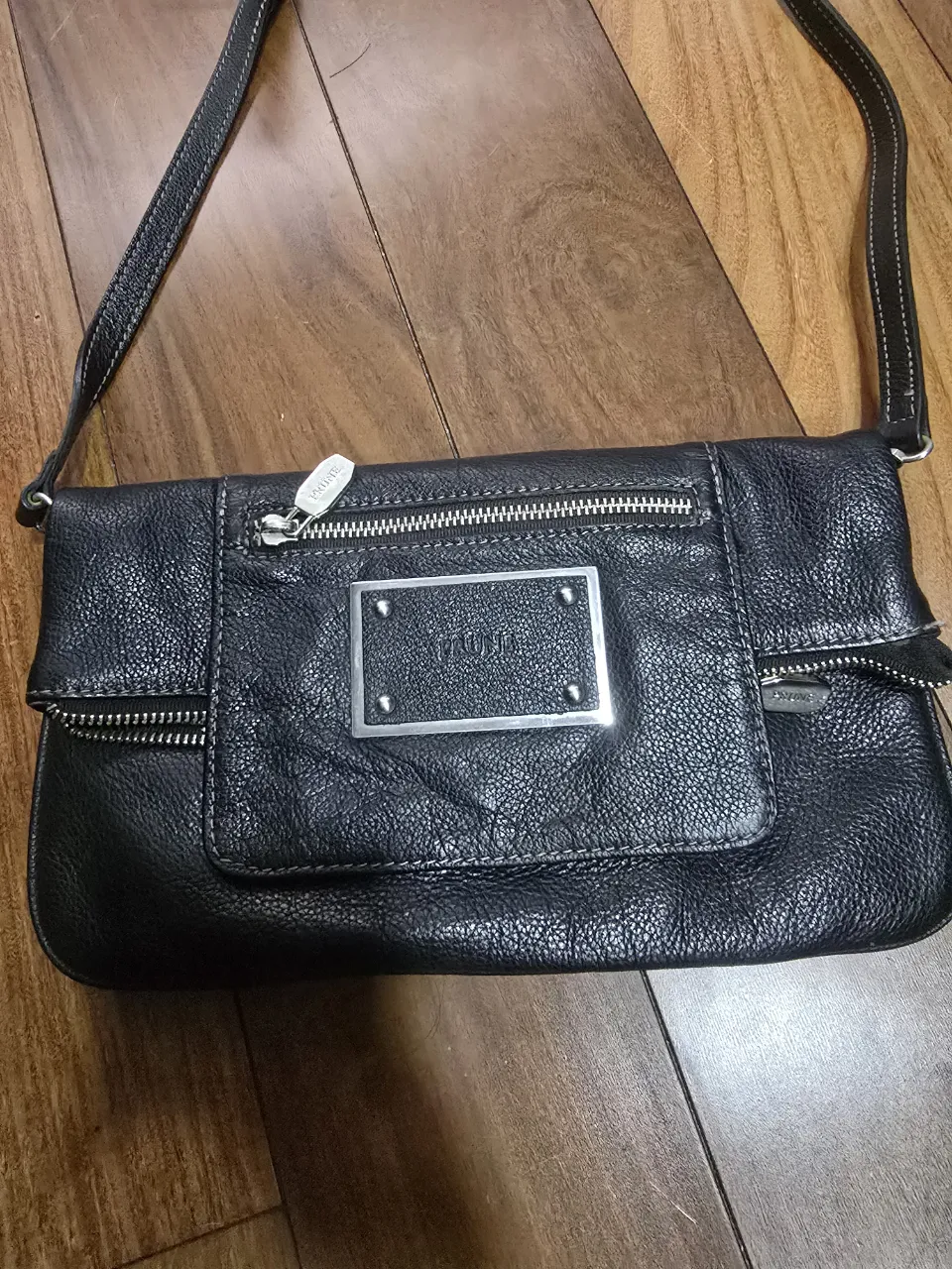 Cartera negra de cuero con correa larga ajustable. impecable. Posee múltiples bolsillos con cierre metálico y un bolsillo frontal con tapa y dos remaches.