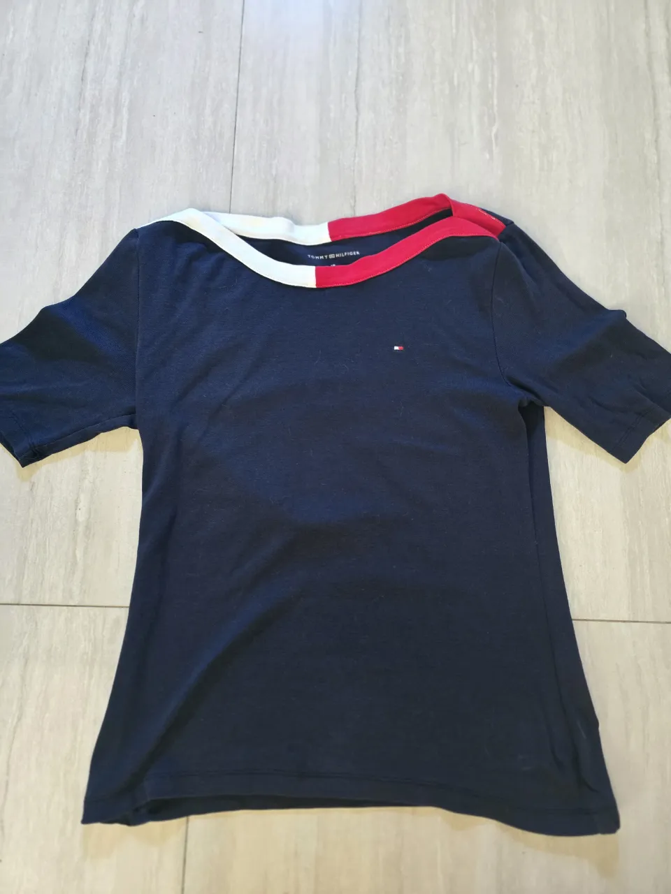 Remera azul marino de manga corta con cuello redondo y detalles en blanco y rojo. Posee un pequeño logo de la marca en el frente. Ideal para un look casual y cómodo.