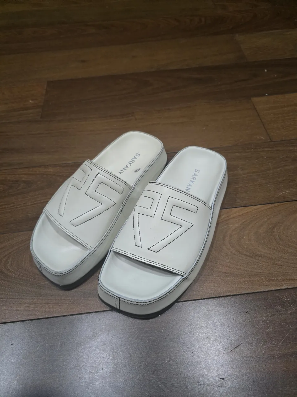 Ojotas blancas de plataforma con diseño de logo en relieve y costuras al tono. Ideales para un look casual y cómodo.