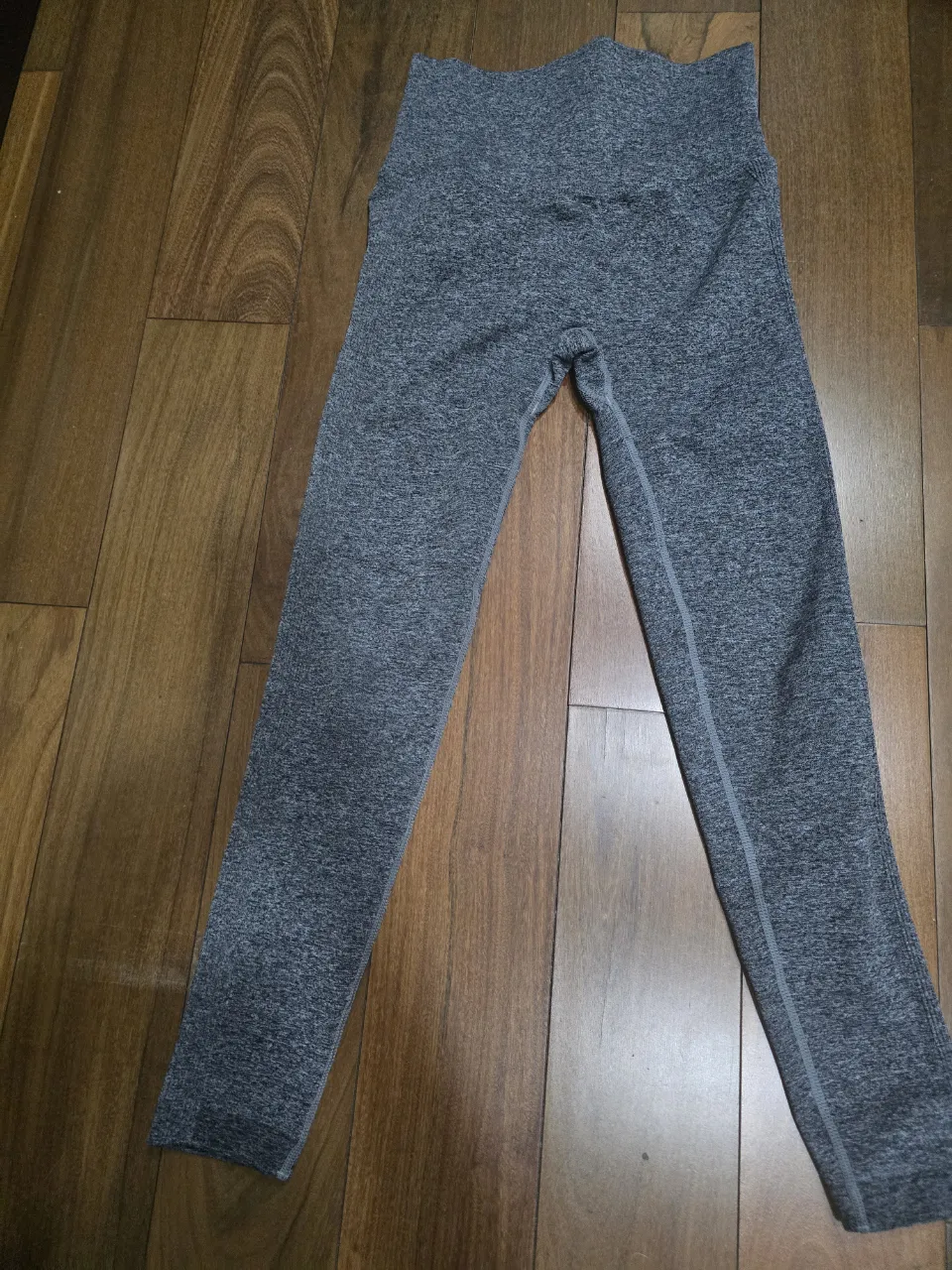 Calzas deportivas grises jaspeadas con costura central en la parte delantera de las piernas. Tienen un logo blanco en la parte trasera superior.