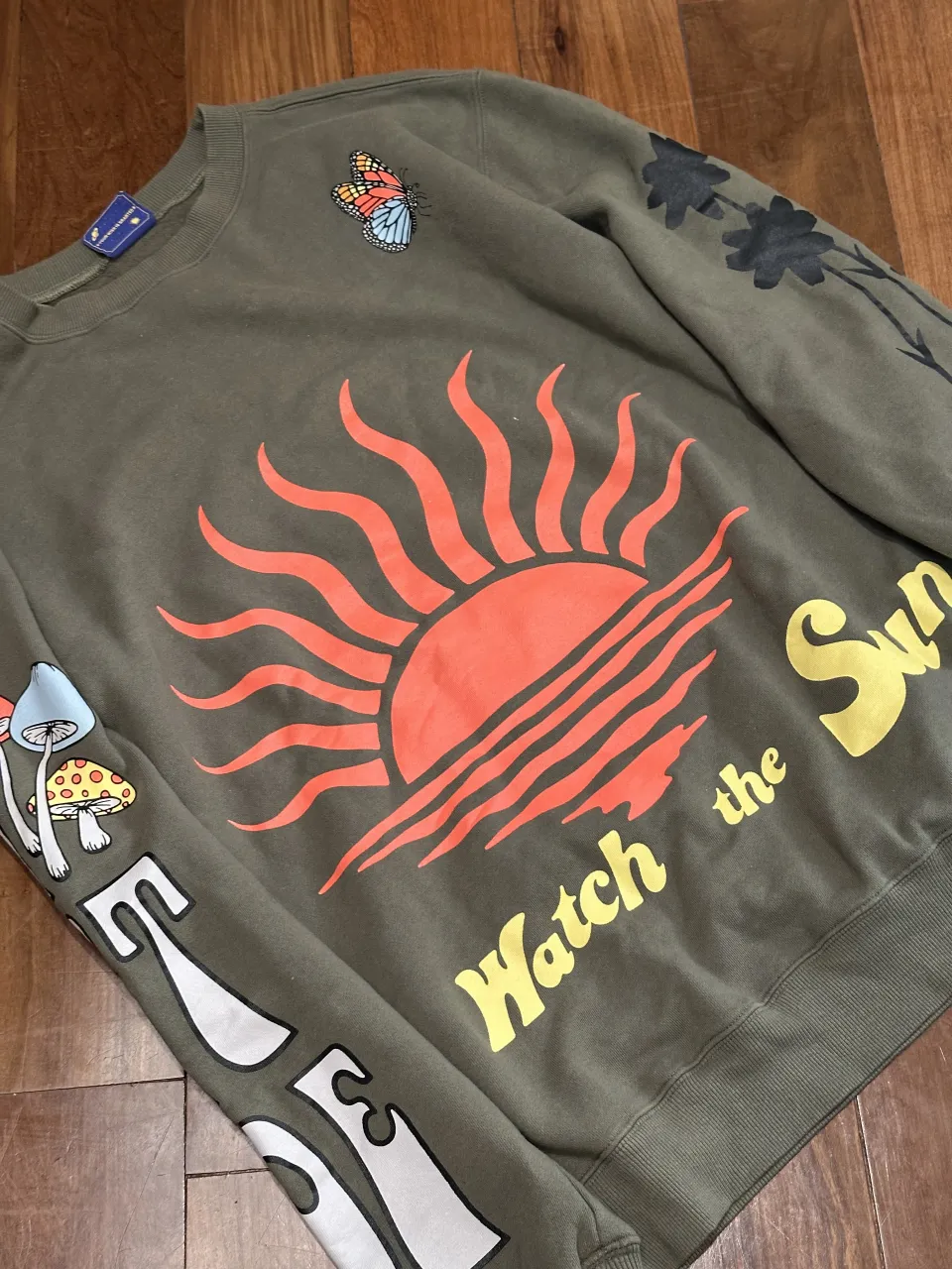 Buzo de algodón color verde militar con estampa de sol y olas en el frente. En las mangas tiene estampas de hongos y mariposa. En la espalda tiene la frase "GET SOME FRESH".