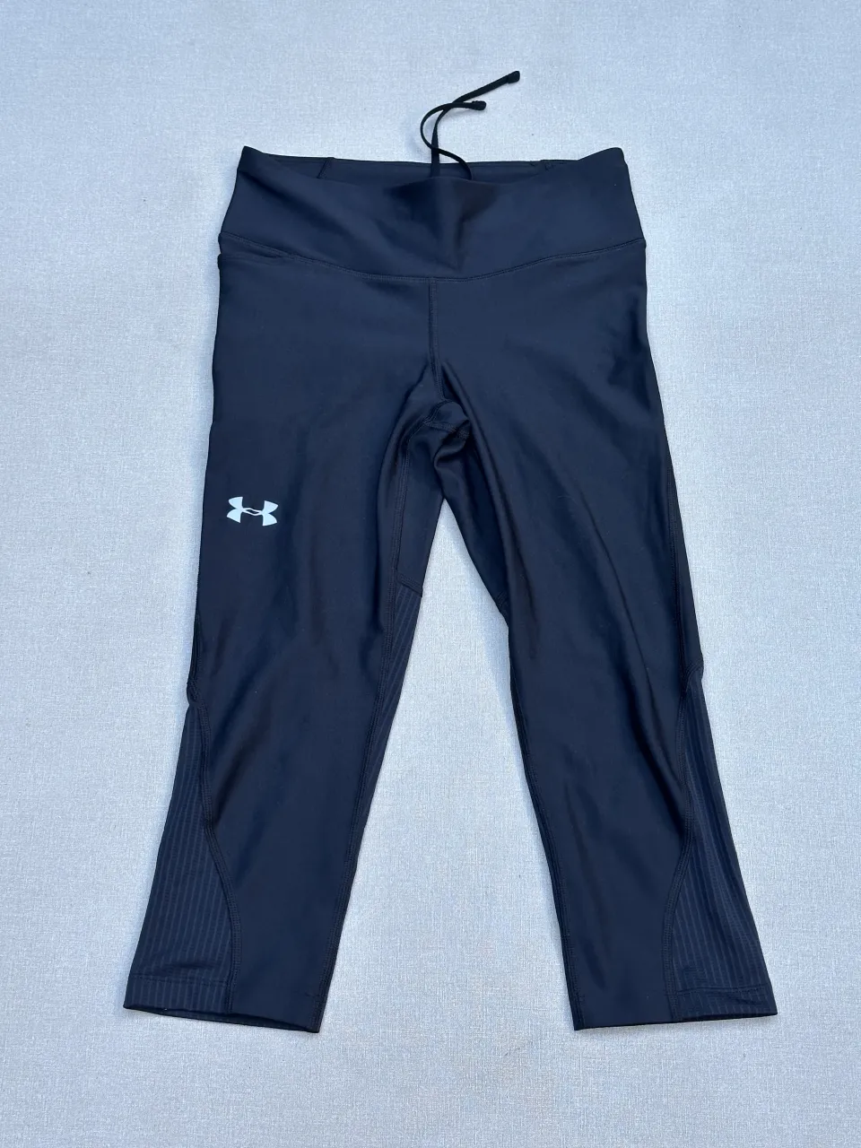 Calzas deportivas capri de compresión Under Armour HeatGear. Ideales para entrenar, correr o cualquier actividad física. Diseño moderno con detalles de textura en las piernas y cordón ajustable en la cintura para un calce perfecto. Comodidad y rendimiento garantizados.