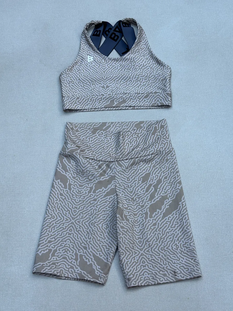 Conjunto deportivo de top y shorts de lycra con estampa abstracta en tonos beige y blanco. Ideal para entrenamientos o para un look casual y cómodo. Detalle en short. 