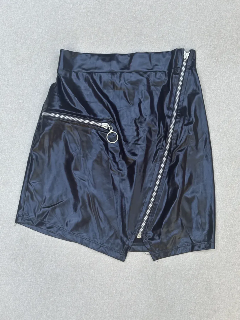 Pollera negra corta, estilo cuero, con detalles de cierre metálico y argolla. Diseño asimétrico y moderno, ideal para looks audaces y cancheros.