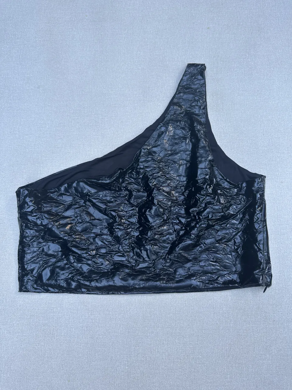 Top negro de cuero sintético con textura arrugada y un solo hombro. Ideal para un look audaz y moderno.