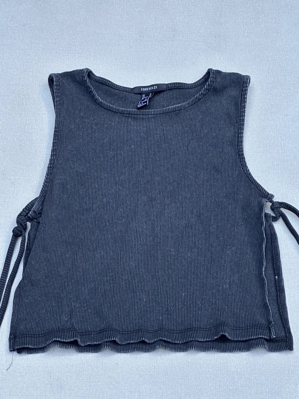 Musculosa crop de algodón acanalado con cordones laterales para anudar. Diseño moderno y canchero, ideal para looks urbanos y casuales.