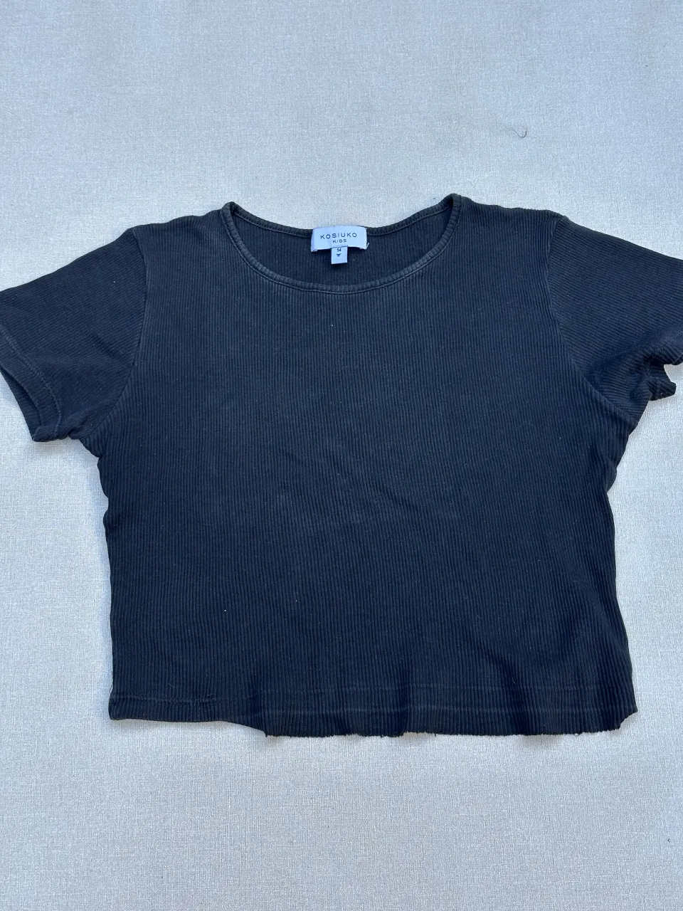 Remera negra de algodón acanalada, con mangas cortas y corte crop. Tiene un bordado sutil en la manga.