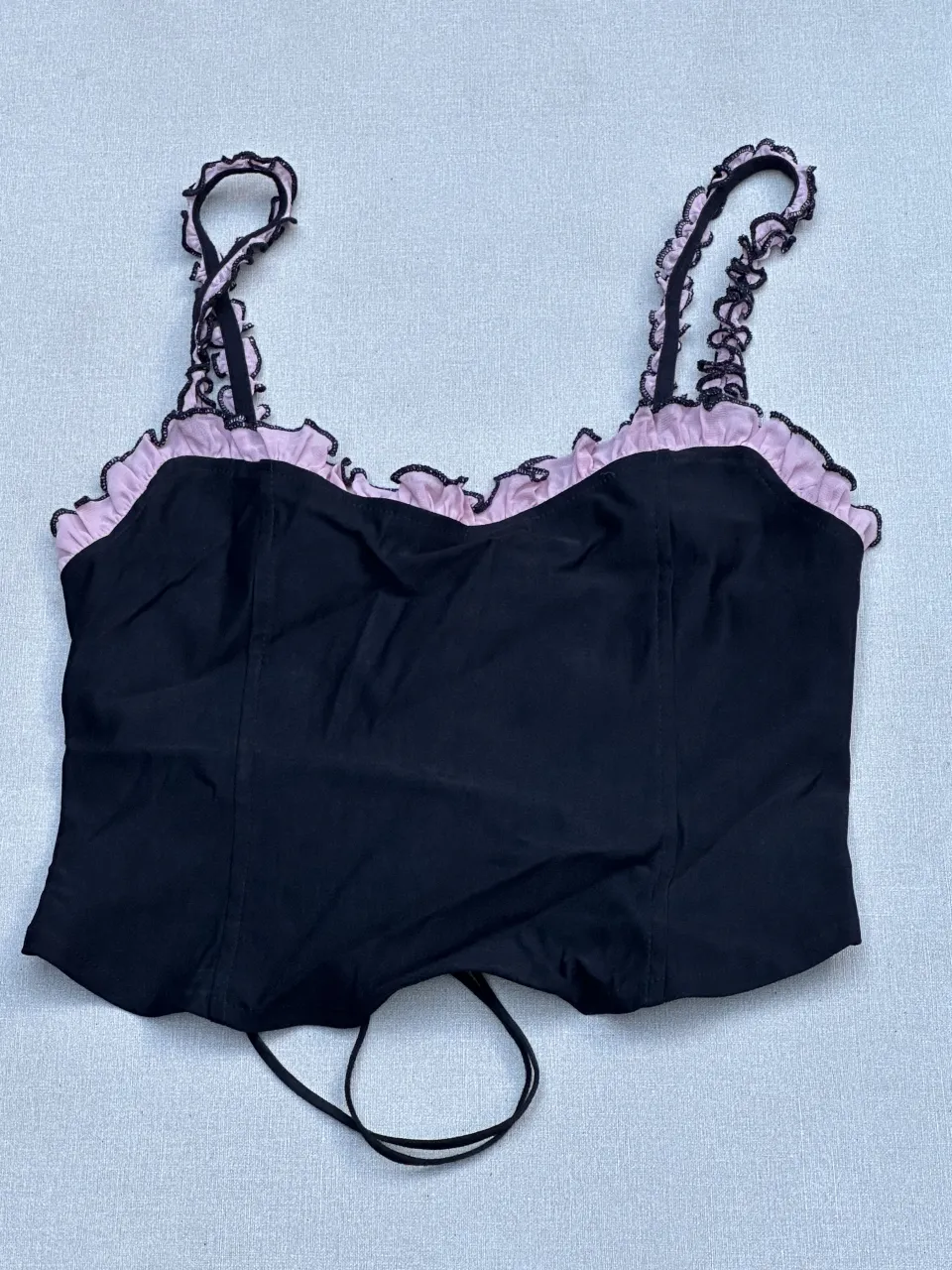 Top negro con detalles en rosa y encaje. Posee tiras finas con volados y un diseño de corset en la espalda con cordones. Ideal para un look canchero y a la moda.