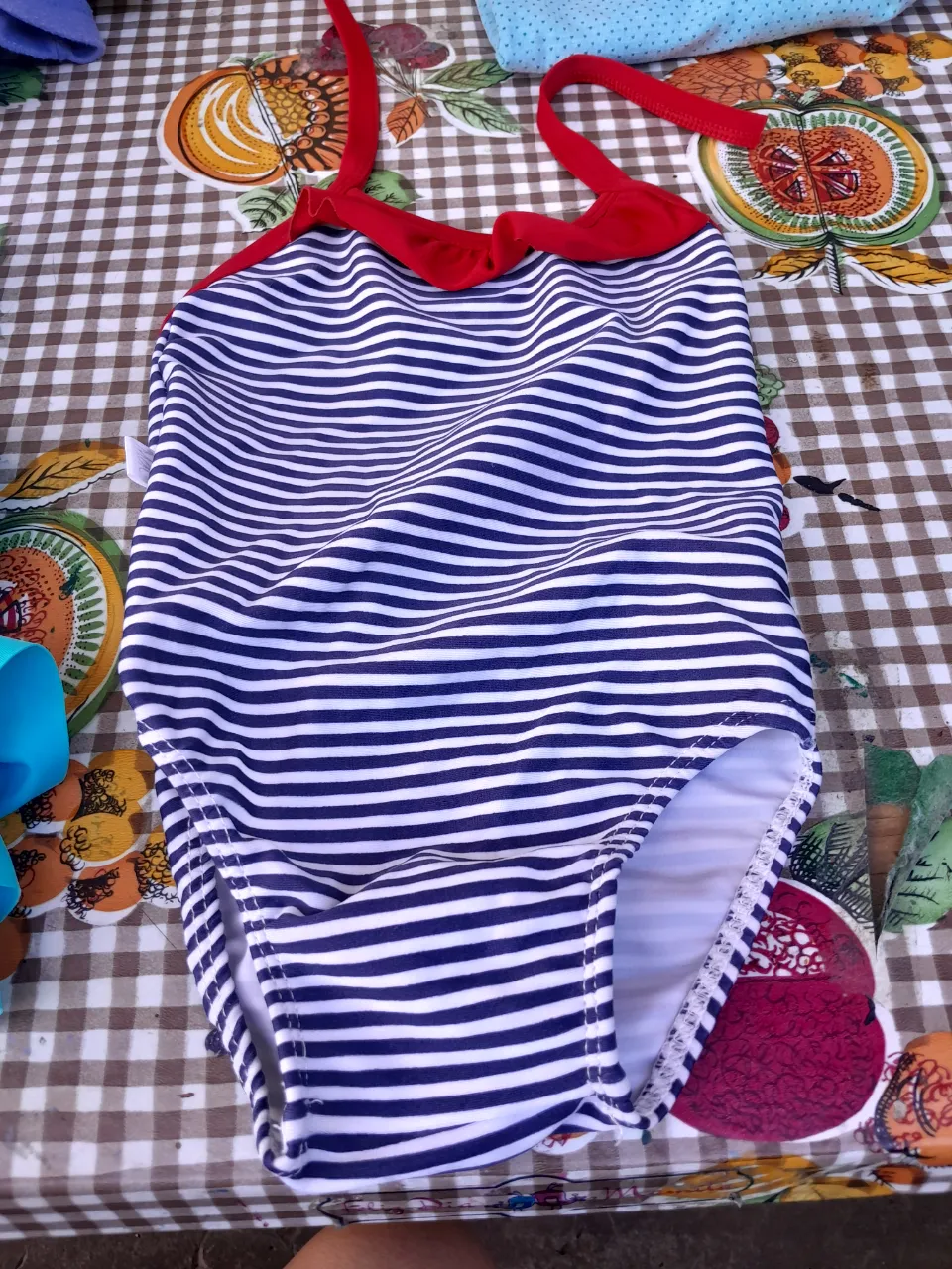 Traje de baño entero a rayas azules y blancas con detalles rojos. El segundo traje de baño es de color turquesa con dos flamencos estampados. El tercer traje de baño es blanco con estampado de hojas tropicales y Minnie Mouse.