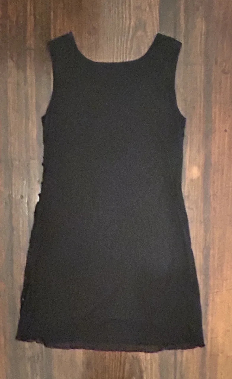 Vestido negro corto, sin mangas, con detalles de diseño en relieve y lentejuelas. Ideal para fiestas y eventos.