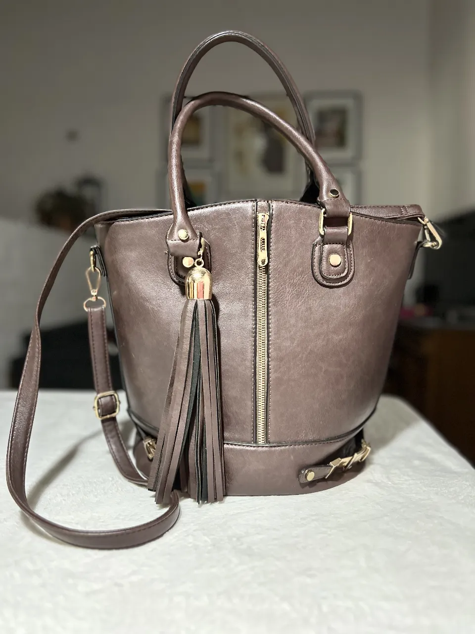 Cartera de mano marrón con detalles dorados, ideal para un look elegante y sofisticado. Cuenta con cierre y correa para llevar al hombro y un bolsillo interno para notebook.
