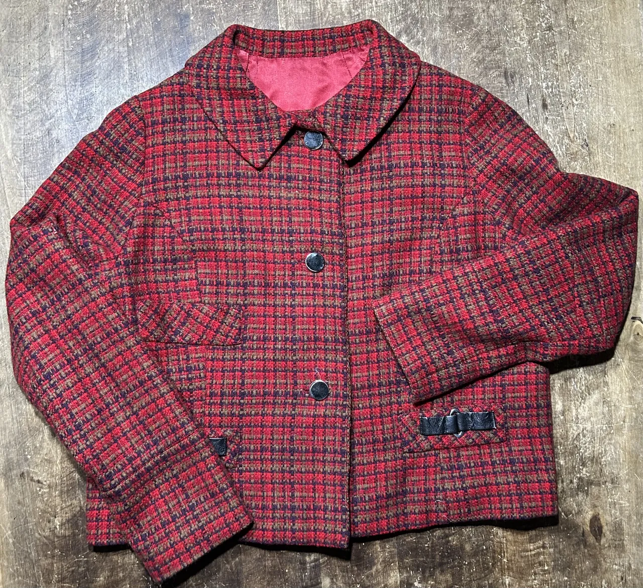 Chaqueta de mujer estilo vintage, con estampado a cuadros en tonos rojos y marrones. Posee dos bolsillos delanteros y detalles de hebillas en las mangas. Ideal para un look retro y sofisticado.
