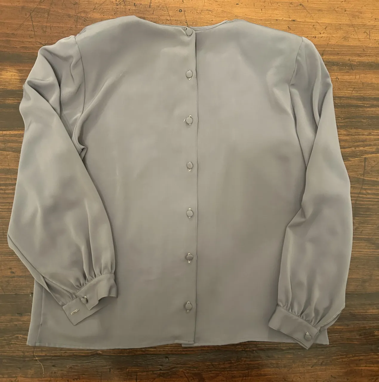 Blusa gris con botones en la parte trasera y mangas largas. Ideal para un look elegante y versátil.