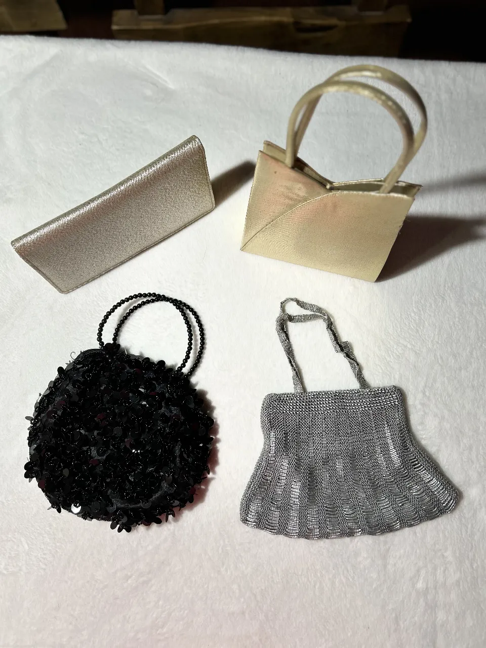 Lote de 4 carteras de diferentes estilos y colores. Incluye una cartera dorada con manijas, una cartera plateada con diseño de canutillos en acero plateado, un clutch plateado y una cartera negra con lentejuelas.