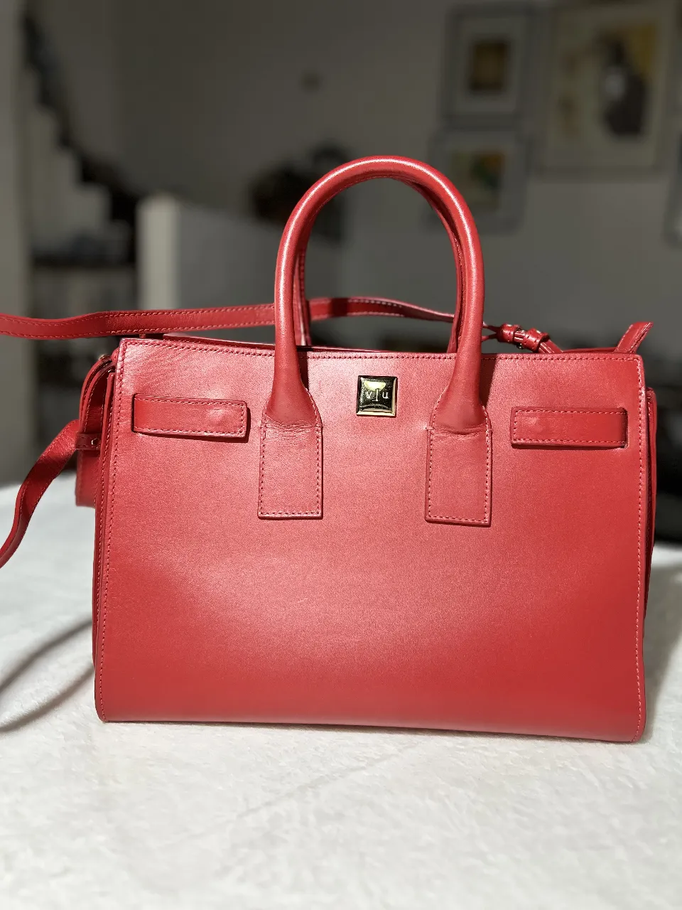 Cartera roja de cuero natural, con manijas cortas y correa larga desmontable. Ideal para llevar tus esenciales con estilo.