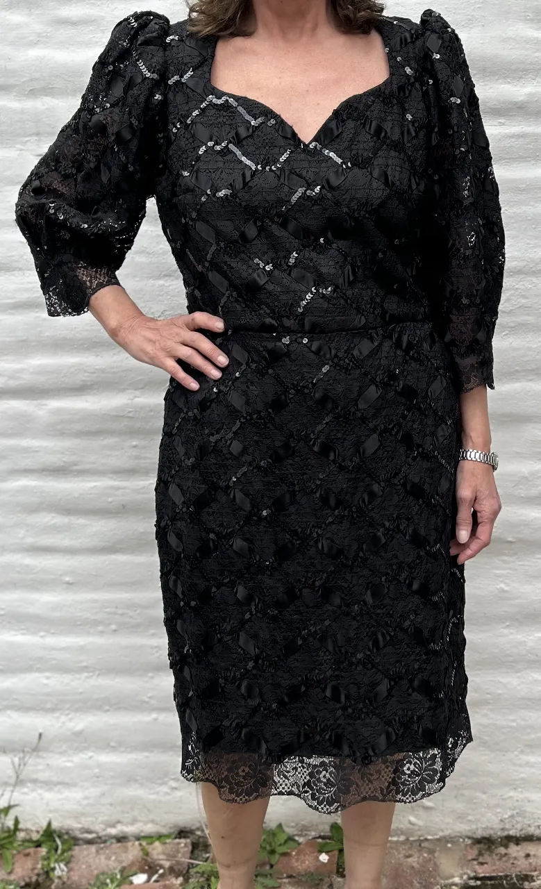 Vestido negro de fiesta, con mangas largas abullonadas y detalles de encaje y lentejuelas. Un diseño elegante y sofisticado, perfecto para eventos especiales.