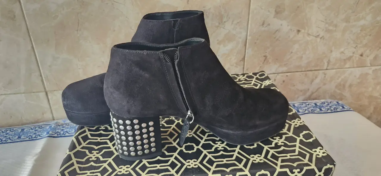 Botines negros de gamuza con taco grueso y detalles de tachas plateadas. Cierre lateral para facilitar el calce. Ideales para un look moderno y canchero.