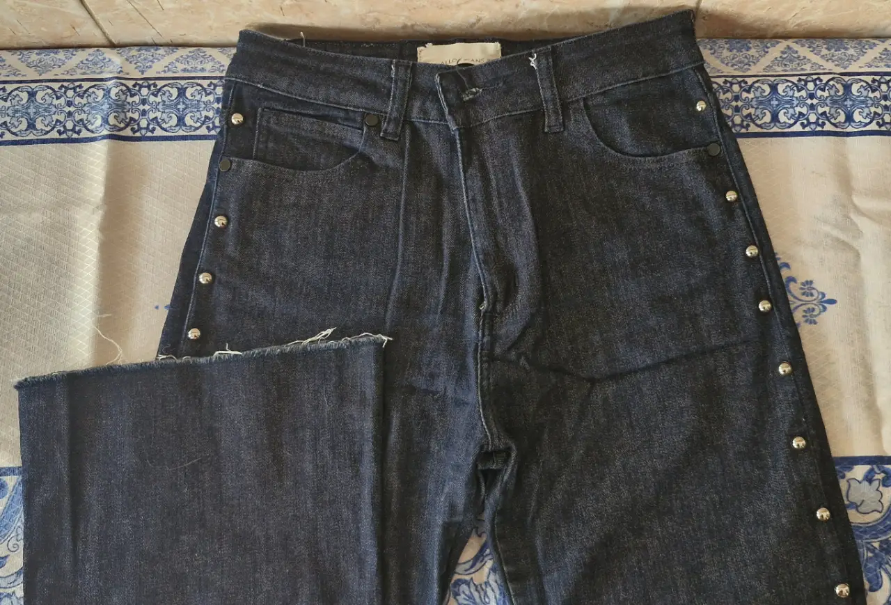 Jeans rectos de denim azul oscuro con detalles de botones plateados en los laterales. Un clásico renovado para un look moderno y versátil.