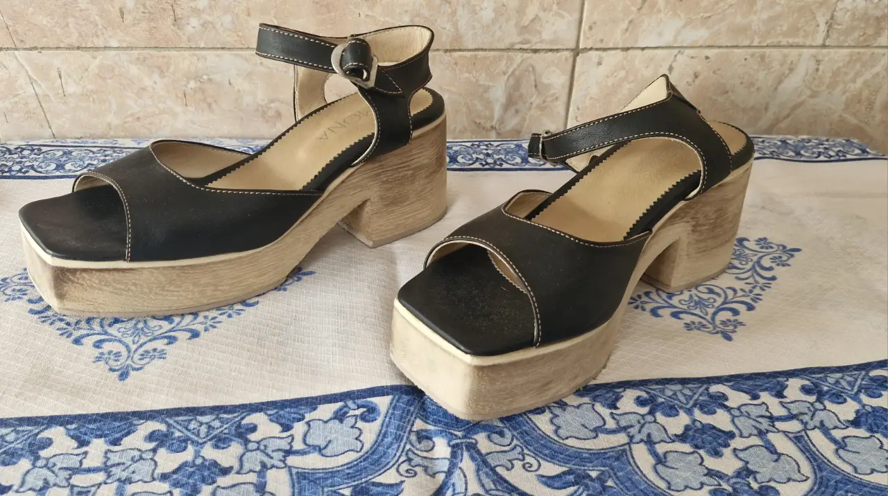 Sandalias de plataforma con base de madera clara y capellada de cuero negro. Diseño con tira en el tobillo y hebilla para un ajuste seguro. Ideales para un look retro y con estilo. super livianos