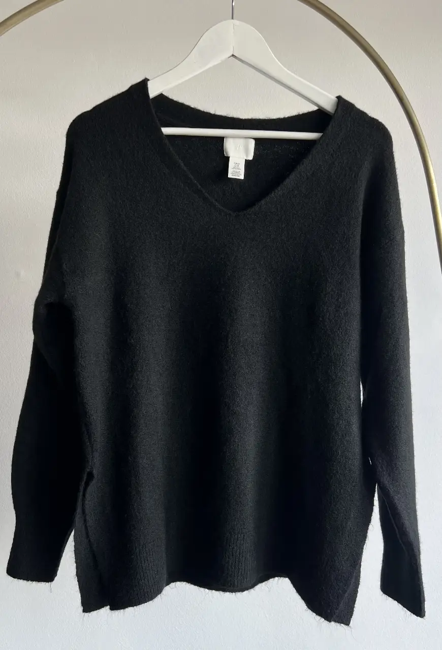 Sweater negro de H&M con cuello en V y aberturas laterales. Talle XS pero oversize ideal para un look casual y cómodo.