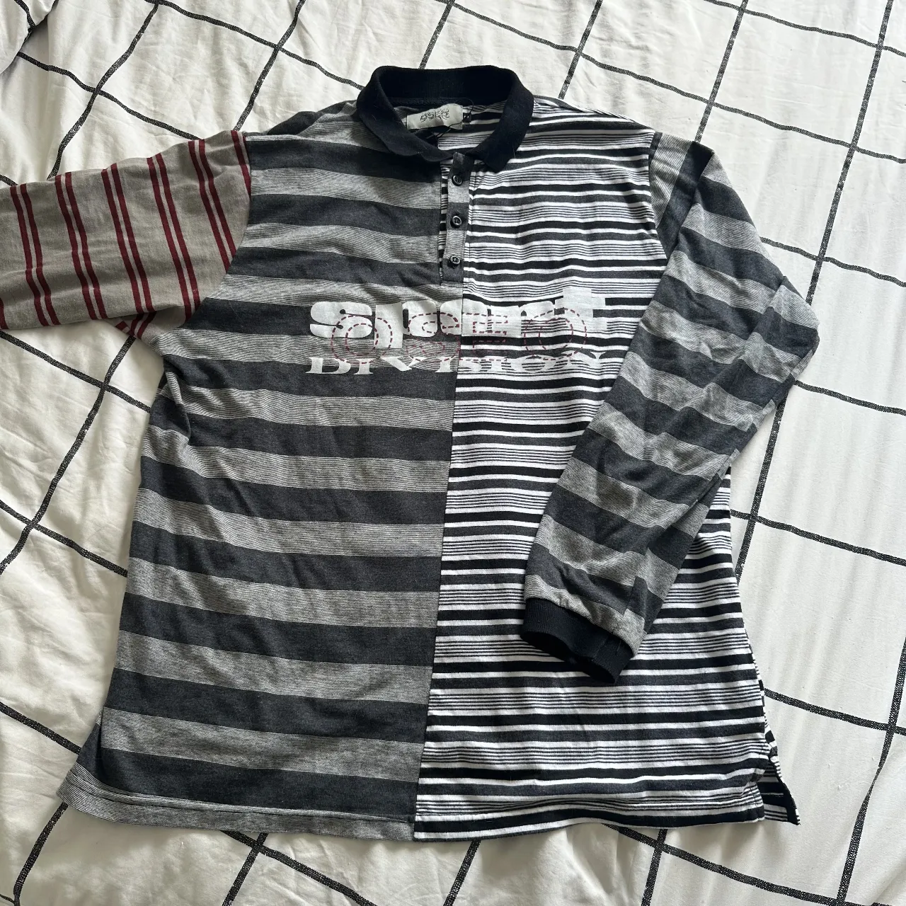 Remera manga larga con un diseño súper original y moderno, mitad a rayas grises y negras, mitad a rayas grises y bordó. Tiene un estampado "Sport Division" en el frente. Ideal para un look urbano y canchero. Es oversize.
