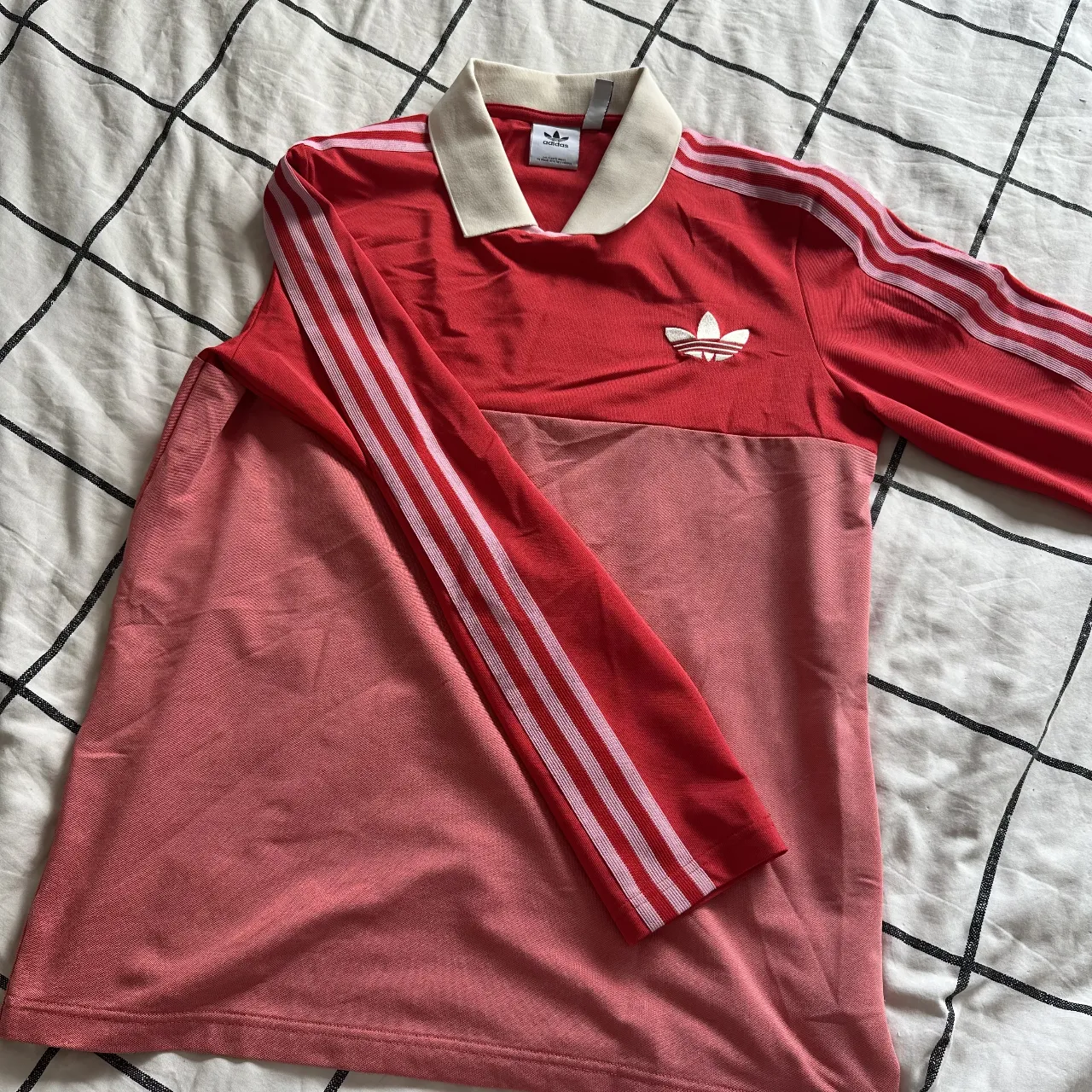 Remera manga larga Adidas, tipo chomba color rojo y rosa, con cuello y las tres tiras icónicas en las mangas. Ideal para un look deportivo y casual.