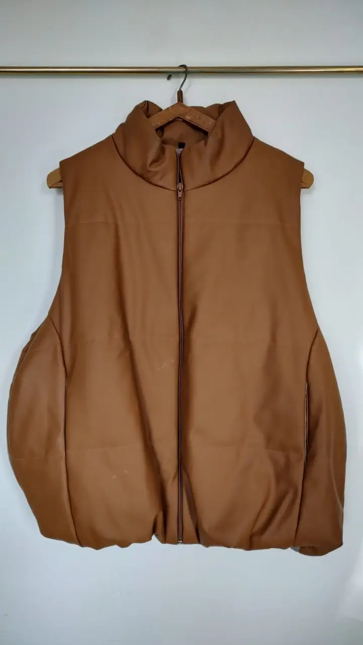 Chaleco puffer de cuero sintético marrón, con cuello alto y cierre frontal. Ideal para un look moderno y abrigado.