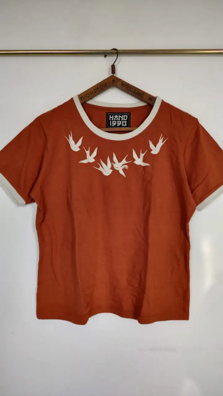Remera manga corta de color naranja con detalles en beige. Diseño con aves bordadas en el frente y detalles en el cuello, espalda y mangas. Ideal para un look casual y con estilo. Está etiquetada como XXL, pero es más bien chico, XL