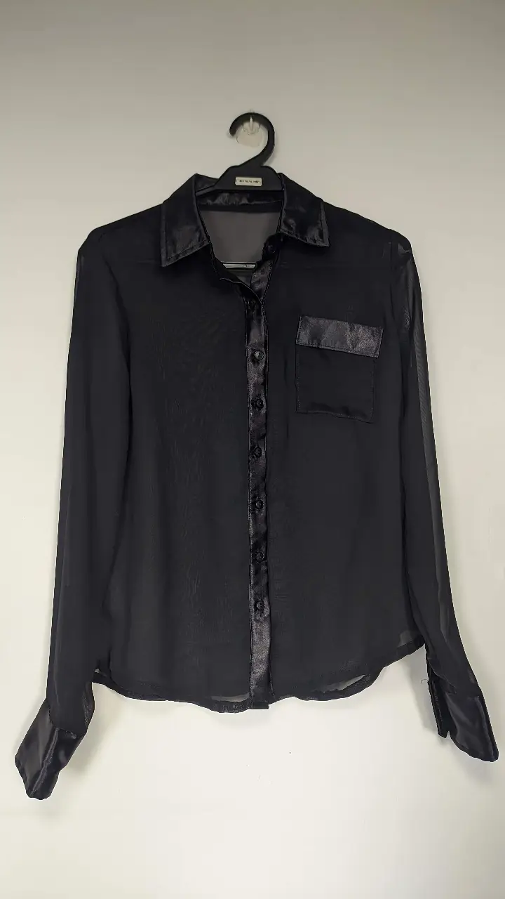 Blusa de mujer negra de seda con detalles de satén. Diseño elegante con bolsillo en el pecho y puños con terminación en satén. Ideal para un look sofisticado.
