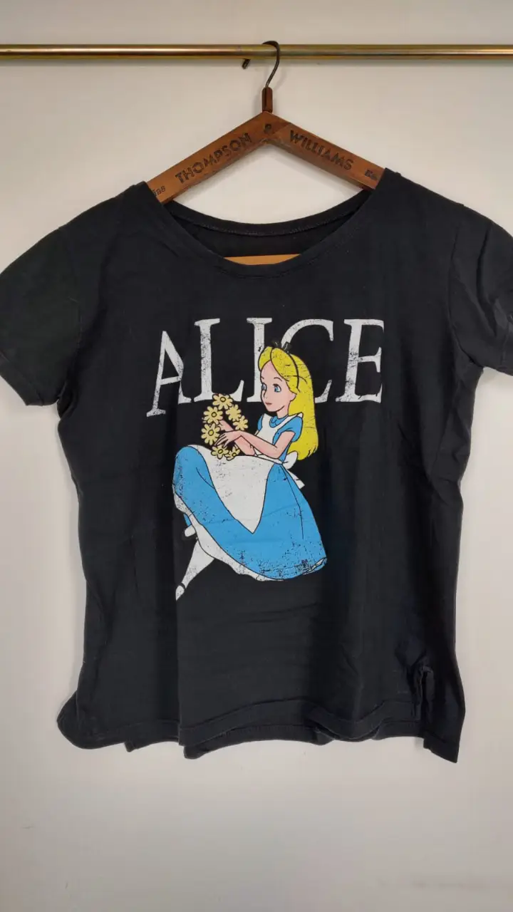 Remera negra de algodón con estampado de Alicia en el país de las maravillas. Diseño vintage con la imagen de Alicia y la palabra "ALICE" en letras blancas. Ideal para un look casual y con onda. Talle único, equivale a S/M