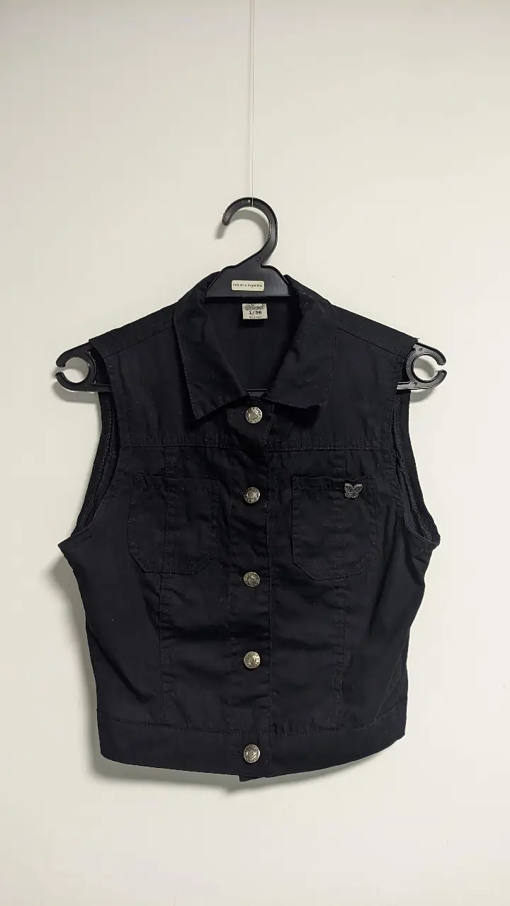 Chaleco negro de gabardina, con botones plateados y detalle de mariposa. Ideal para un look casual y canchero.