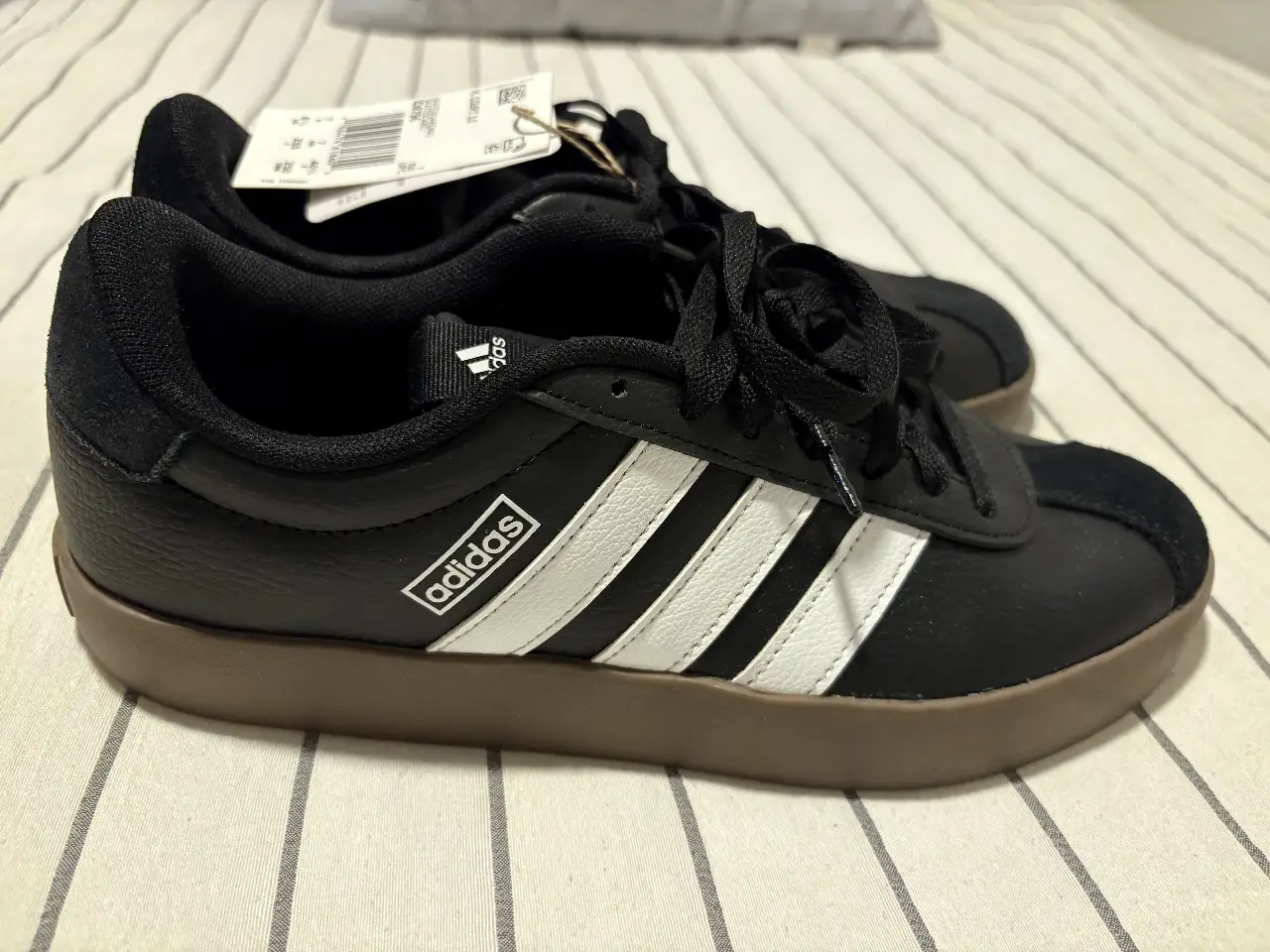 Zapatillas Adidas negras con detalles blancos y suela marrón. Ideales para un look casual y cómodo.