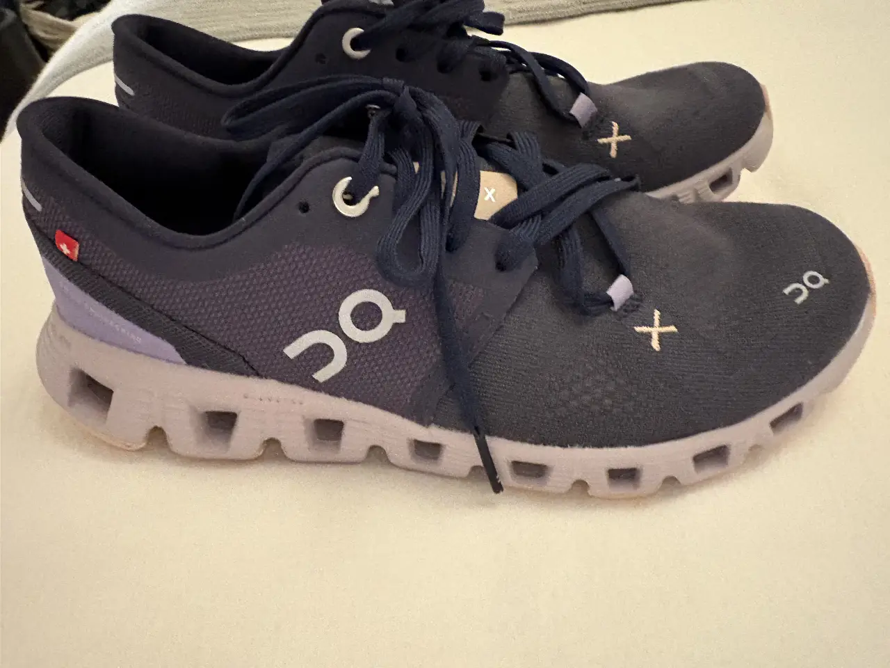 Zapatillas On Cloud X para mujer, color azul marino con detalles en gris y rosa. Ideales para running y entrenamiento, con diseño moderno y tecnología CloudTec para mayor comodidad y amortiguación.