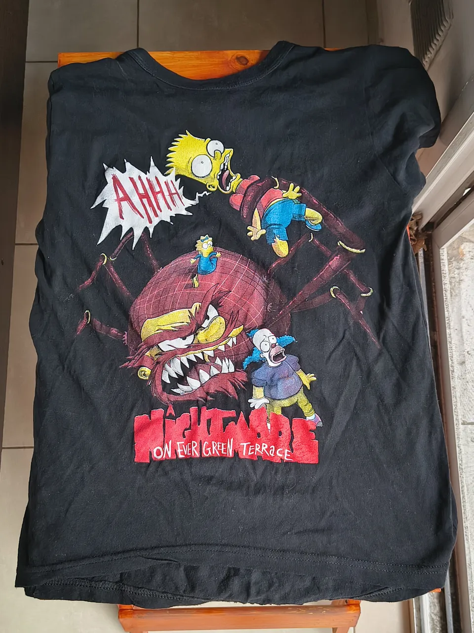 Remera negra de manga corta con estampa "Nightmare on Evergreen Terrace" de Los Simpsons. Ideal para fans de la serie y para un look casual y divertido.