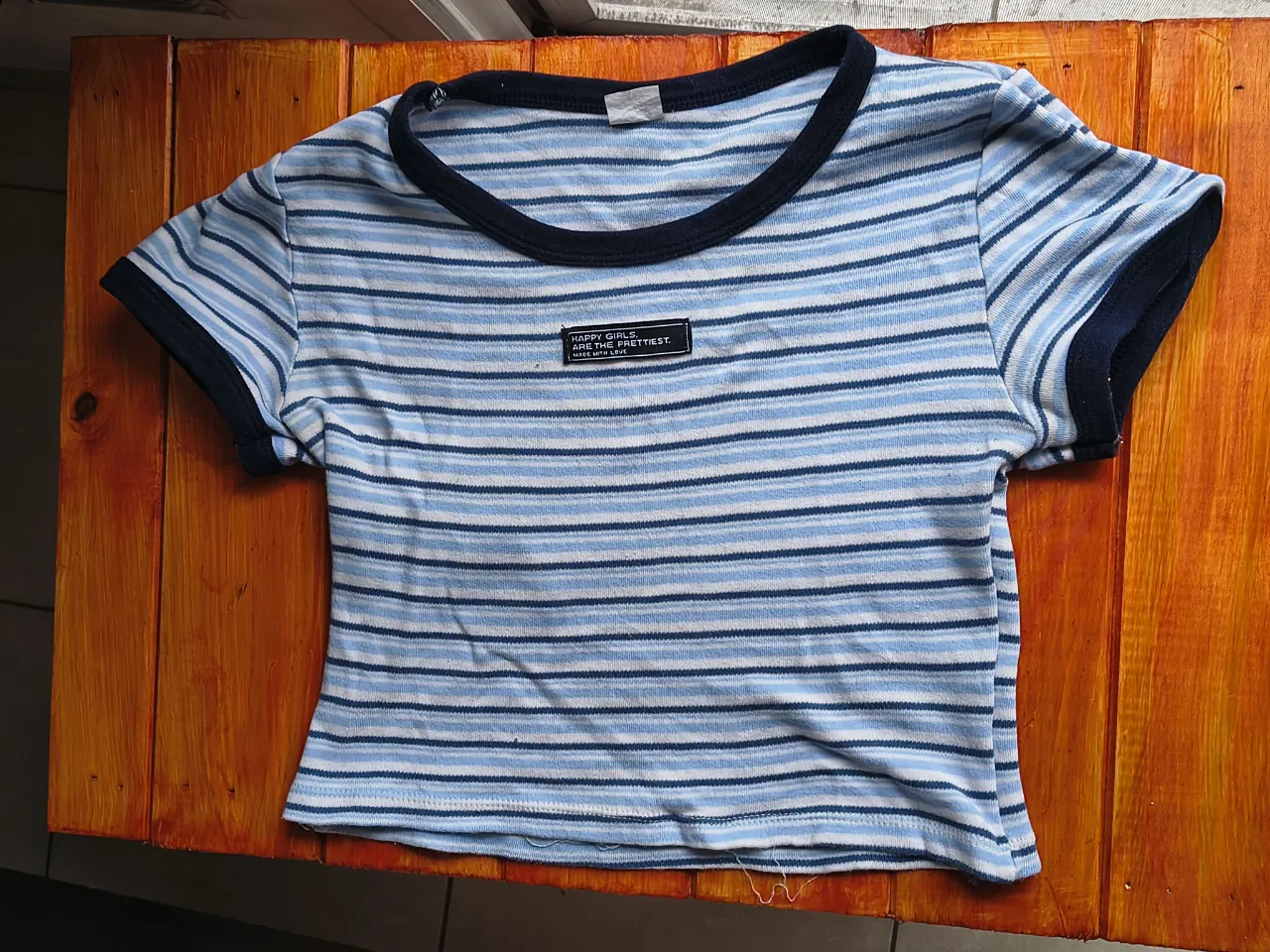 Remera a rayas azules y blancas, estilo crop top. Tiene un detalle de estampa en el frente con la frase "HAPPY GIRLS, ARE THE PRETTIEST. MADE WITH LOVE". Ideal para un look casual y canchero. Talle L, pero banca M o S pero suelto