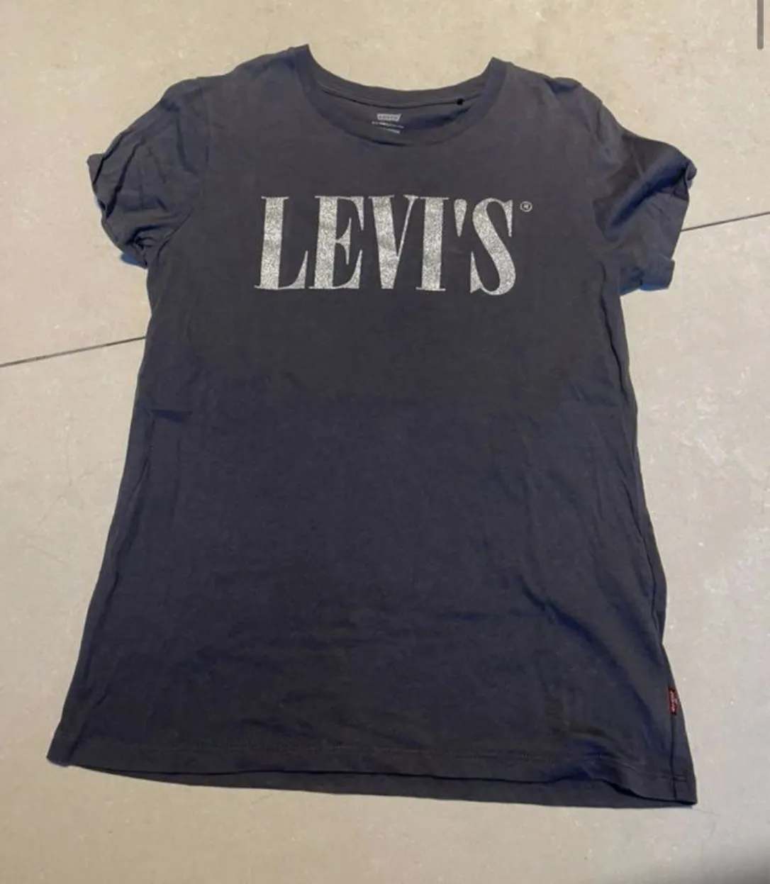 Remera de mujer de color gris oscuro con estampado "LEVI'S" en la parte delantera. Ideal para un look casual y cómodo.
