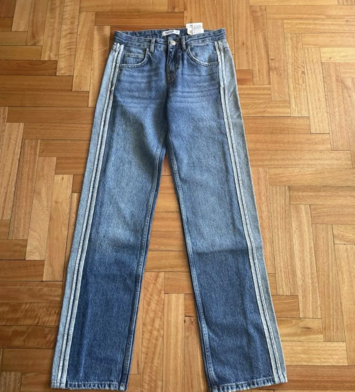 Jeans rectos de mujer, tiro medio, con detalle de franjas laterales en gris claro. Un clásico renovado para un look casual y moderno.