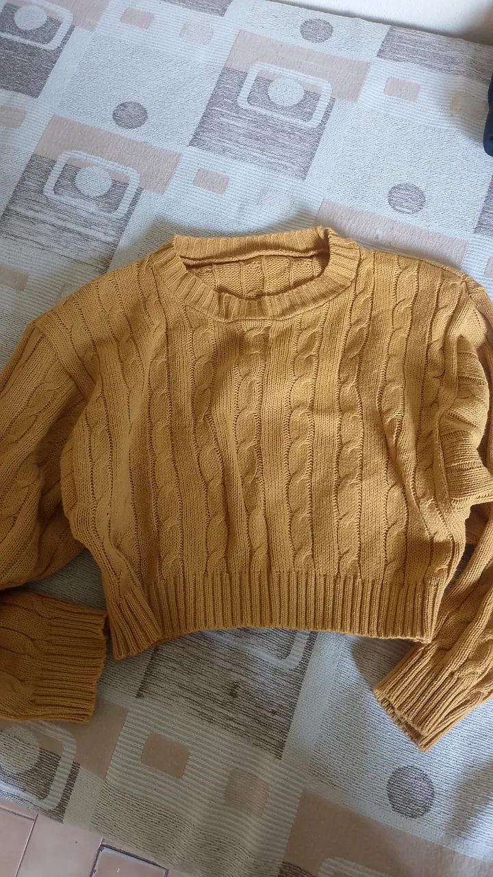 Sweater tejido color mostaza con trenzas, escote redondo y mangas largas. Es un modelo crop, ideal para un look casual y moderno.