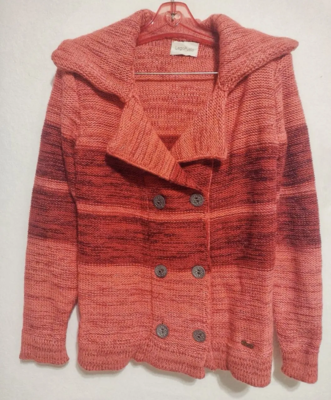 Cardigan tejido a rayas en tonos de coral y bordó. Posee cuello solapa y doble abotonadura con botones grises. Ideal para un look casual y abrigado.