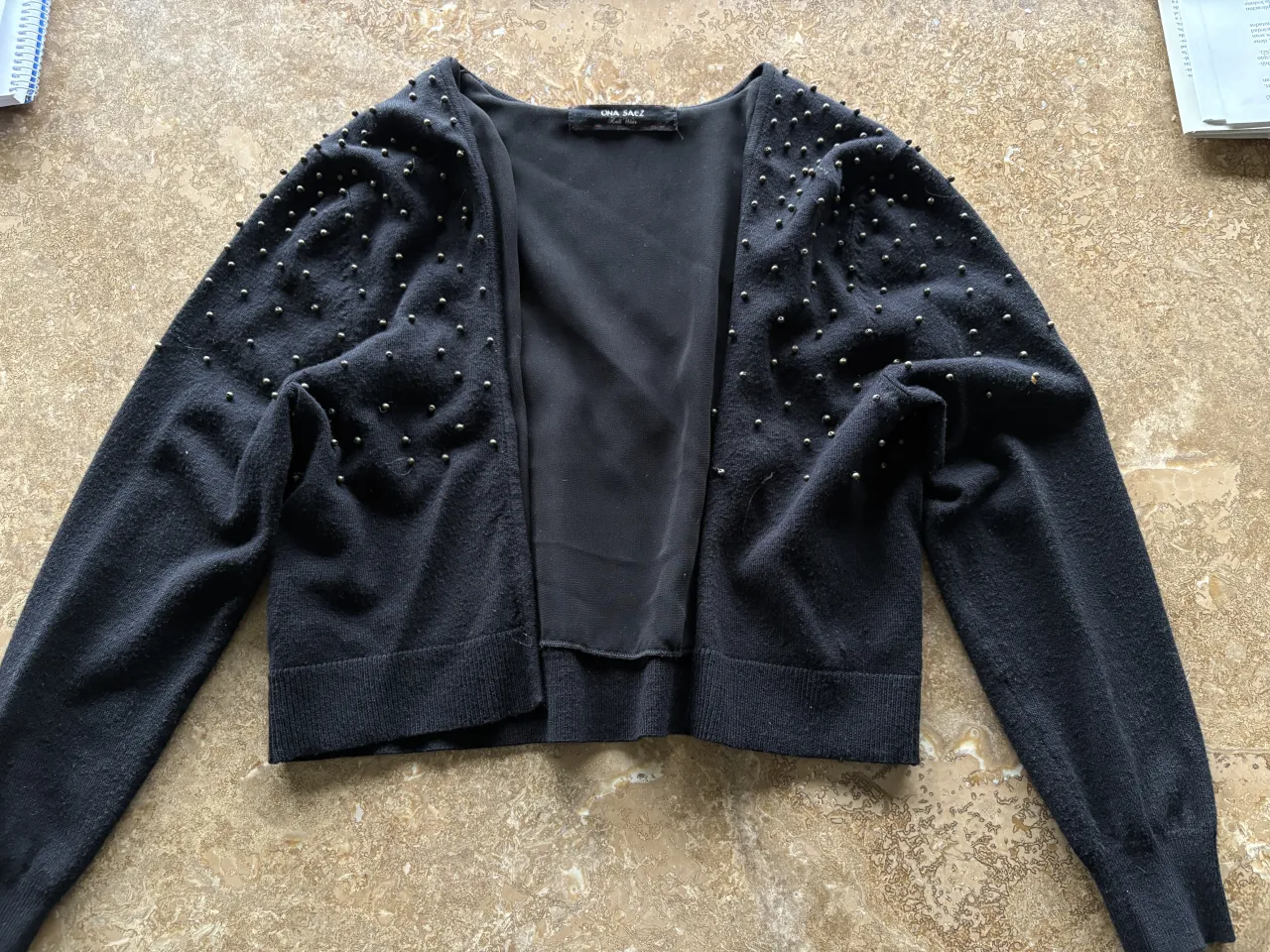 Cardigan negro con tachas plateadas en toda la prenda. Manga larga y escote en V.