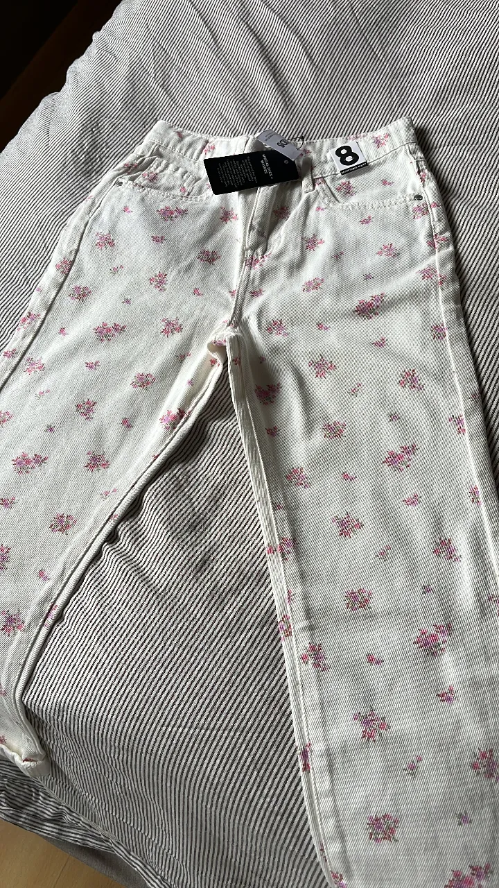 Jeans rectos de mujer con estampado floral en tonos rosas sobre fondo blanco. Talle 8, ideal para un look casual y fresco.