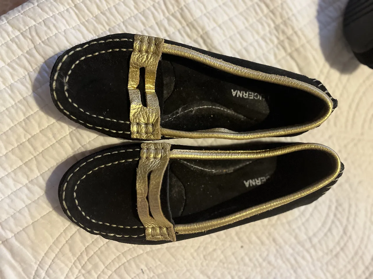 Mocasines negros de gamuza con detalles dorados. Ideales para un look elegante y cómodo.