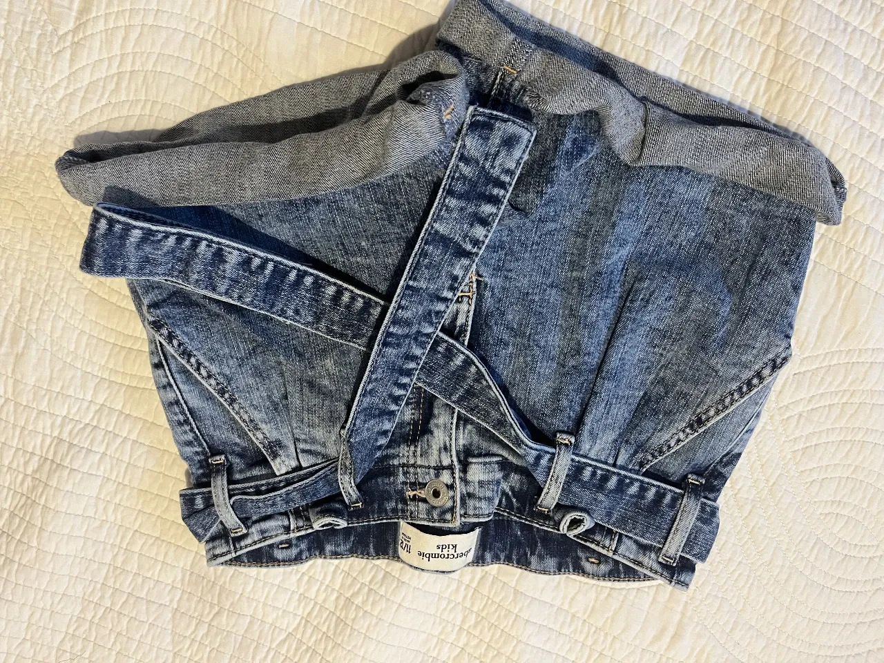 Short de jean azul de la marca Abercrombie Kids, con detalles de desgaste y cinturón. Ideal para un look casual y cómodo.