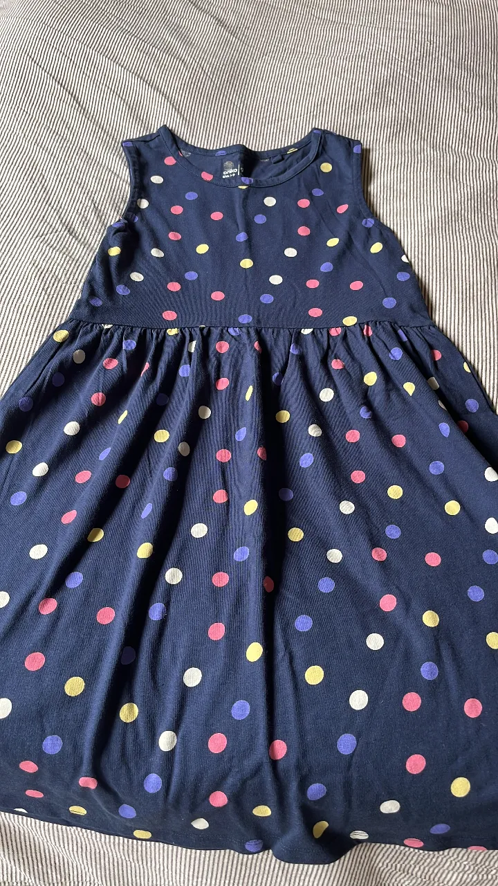 Vestido mini de niña, sin mangas, con estampado de lunares en varios colores sobre fondo azul marino. Ideal para un look casual y fresco.